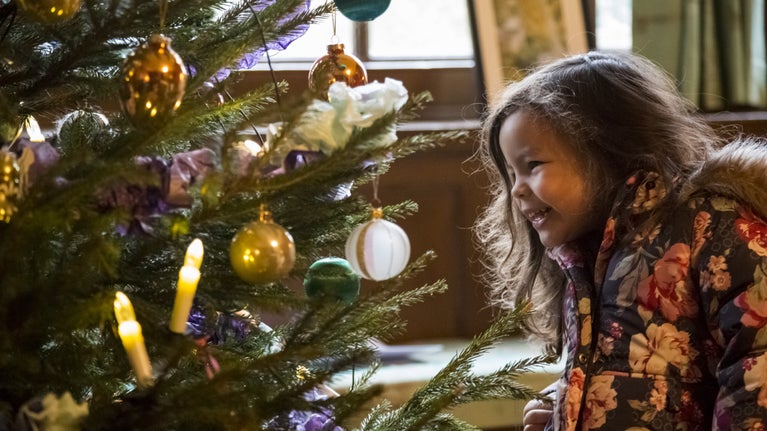 A young girl looking at a large white bauble on a Christmas tree.